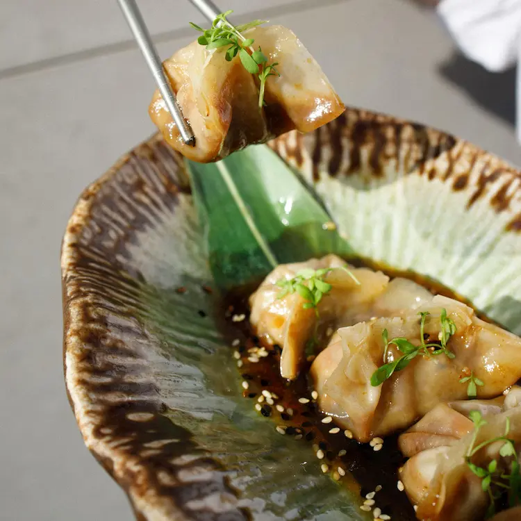 image of a pork gyoza being dipped in soya sauce with chopsticks