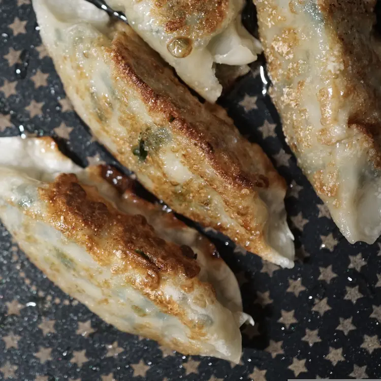image of 4 pork gyozas sizzling in oil on a pan